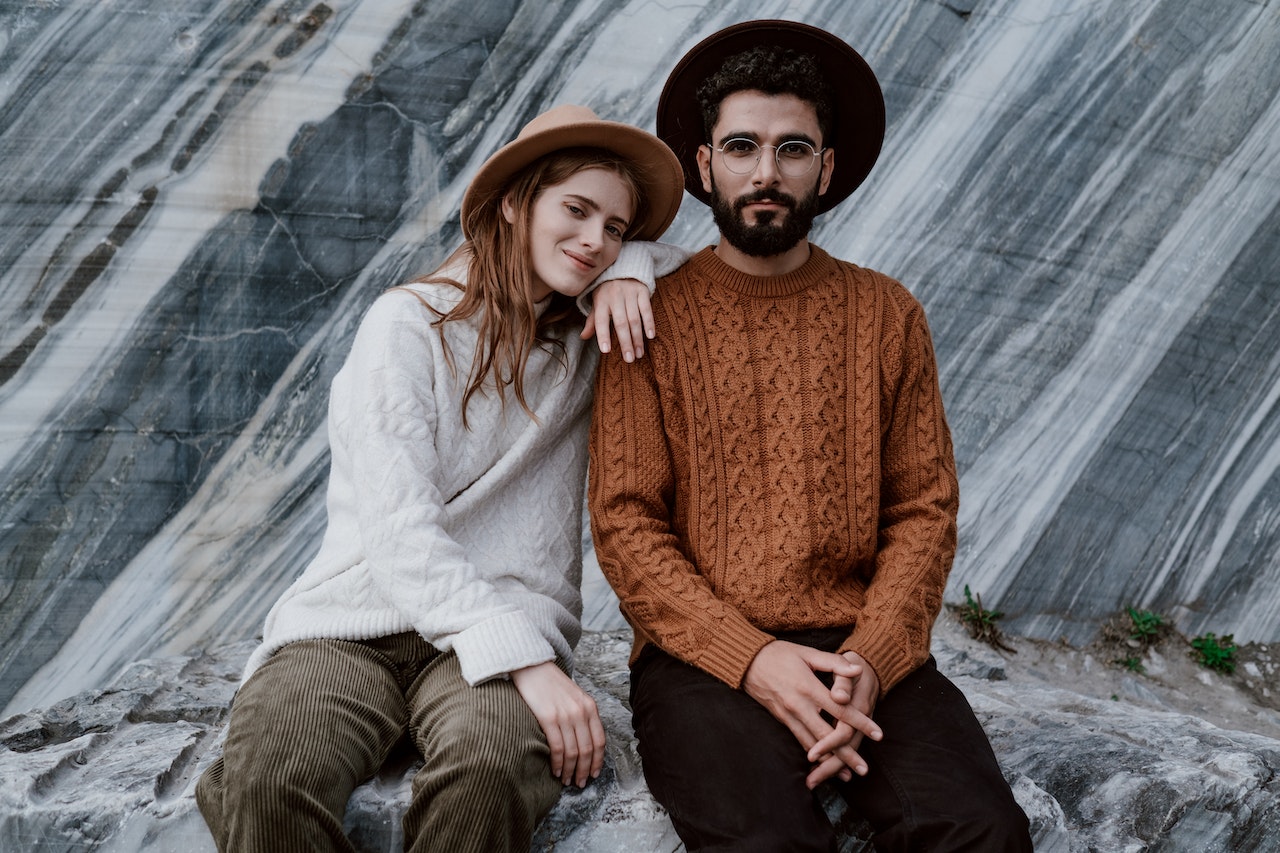 Couple Wearing Knitted Sweaters While Sitting on a Rock Formation