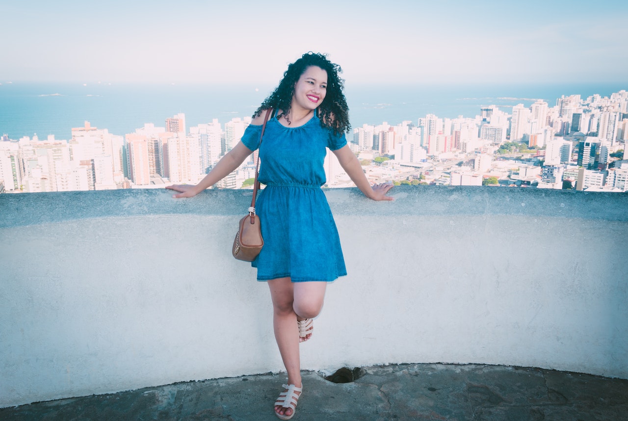 Smiling Woman Wearing A Blue Dress Is Standing on a Rooftop Overlooking The City