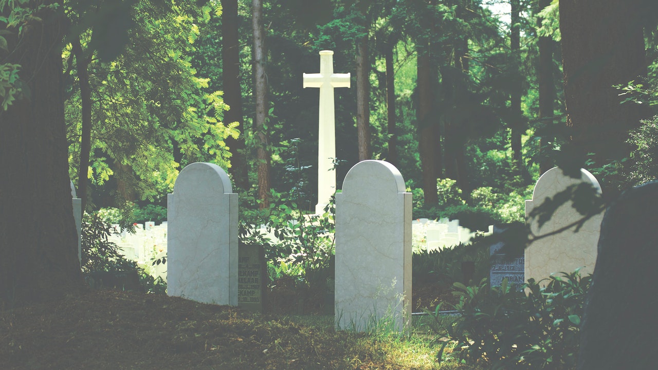 White Tombstones Near Cross Surrounded by Trees