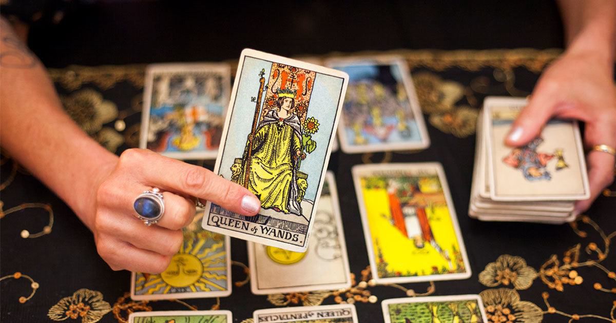 A woman holding the queen of wands tarot card on one hand and a stack of tarot cards on the other hand