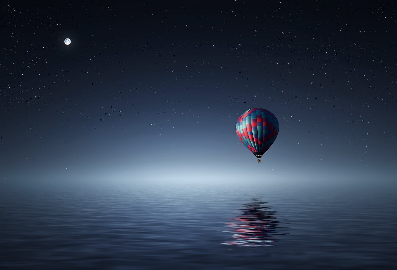 Red and Blue Hot Air Balloon Flying Over the Sea during Night Time