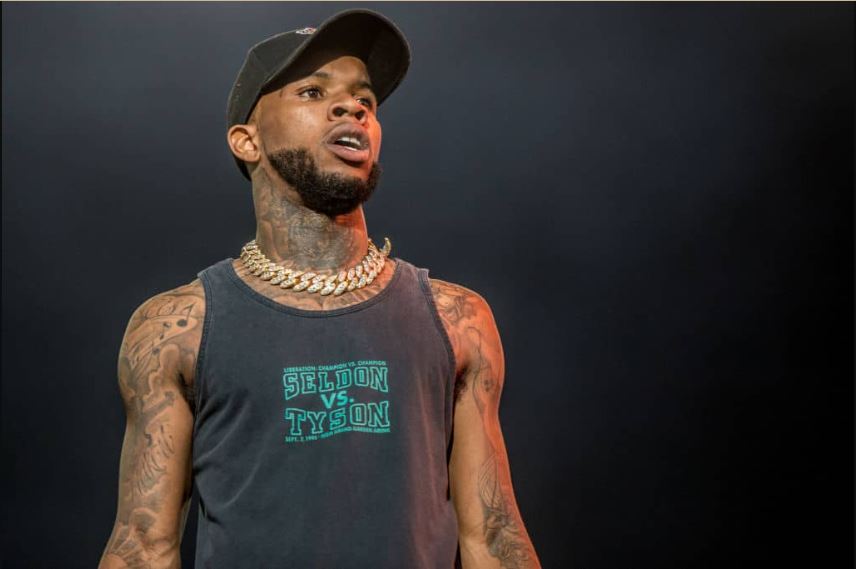 Tory Lanez wearing a black singlet, a big gold necklace, and a black face cap