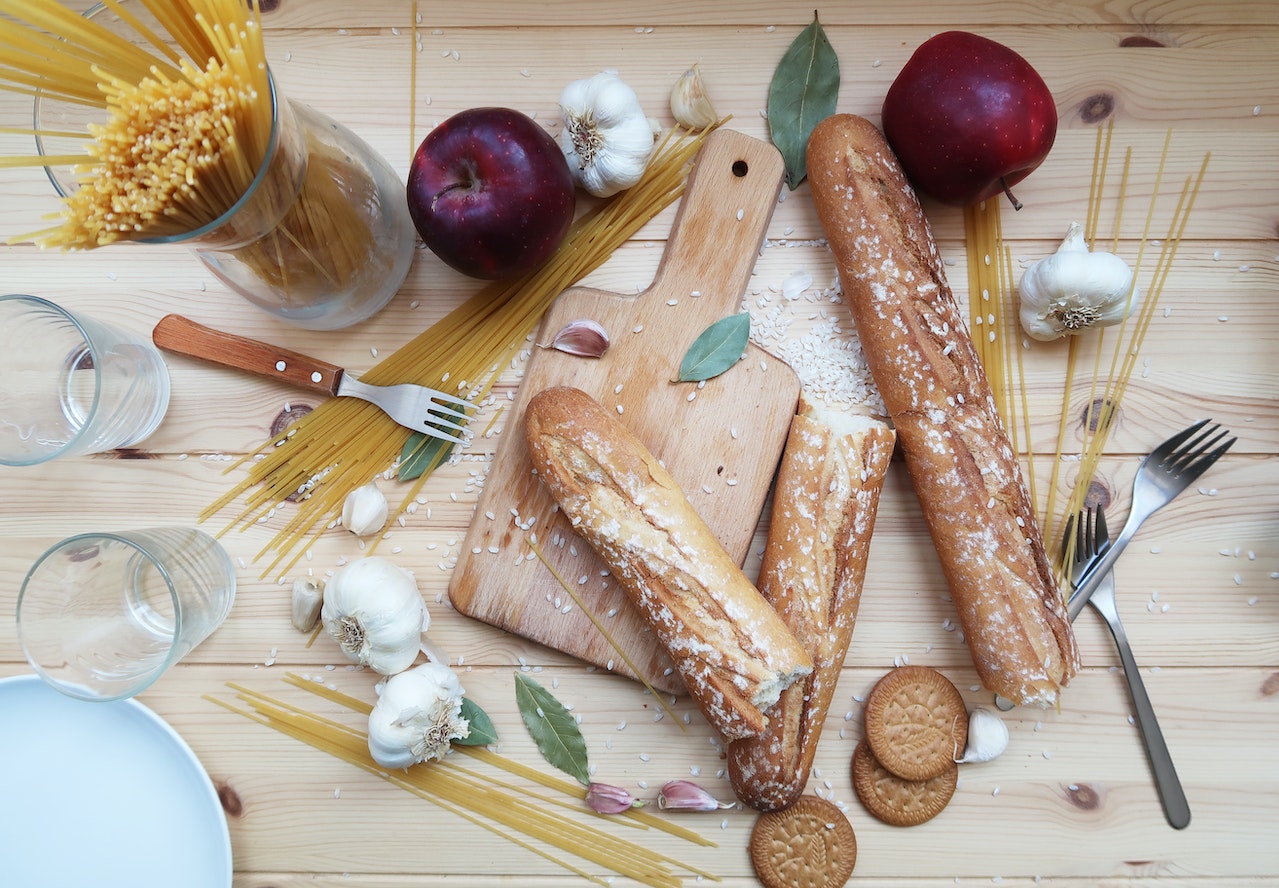 Baguettes, pasta, garlic, cookies, apples, forks, and glasses on a wooden table