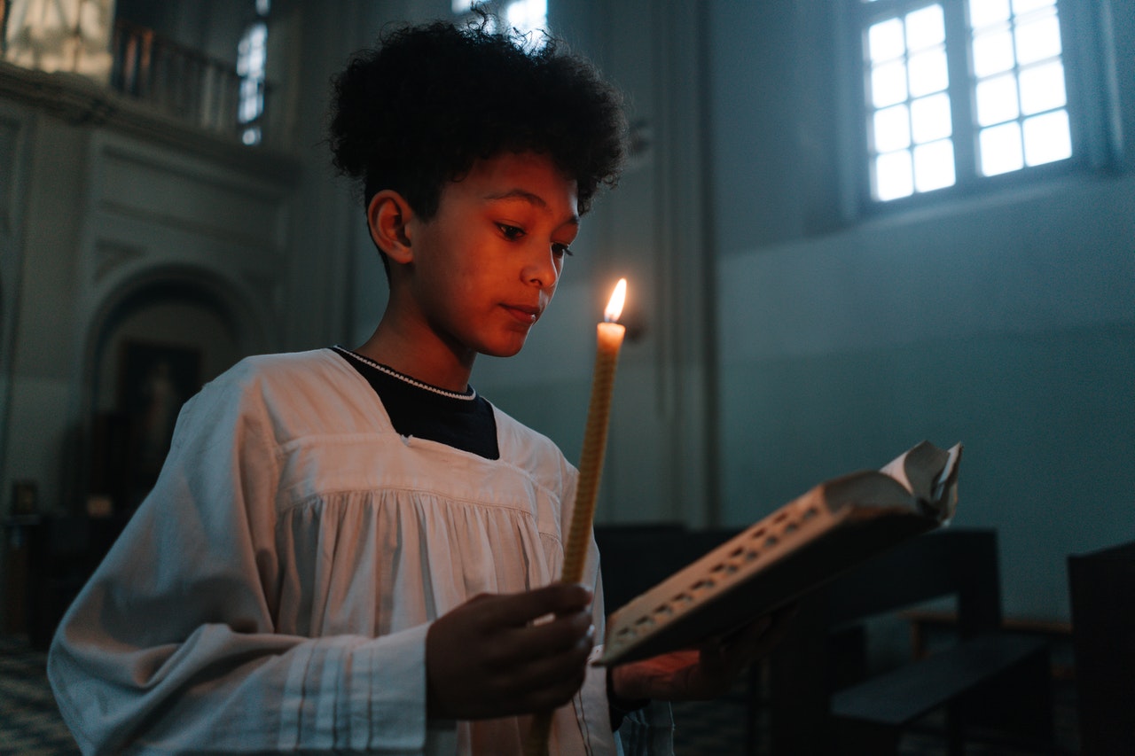 A sacristan holding a candle while reading a Bible