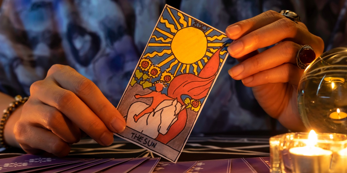 A person holding a sun tarot card with a candle on the side