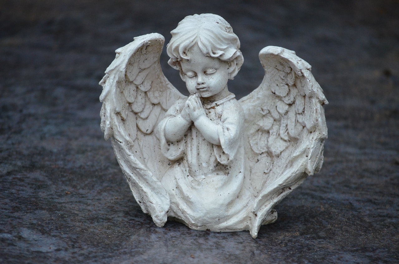 An Angel Statue Kneeling On The Ground While Praying