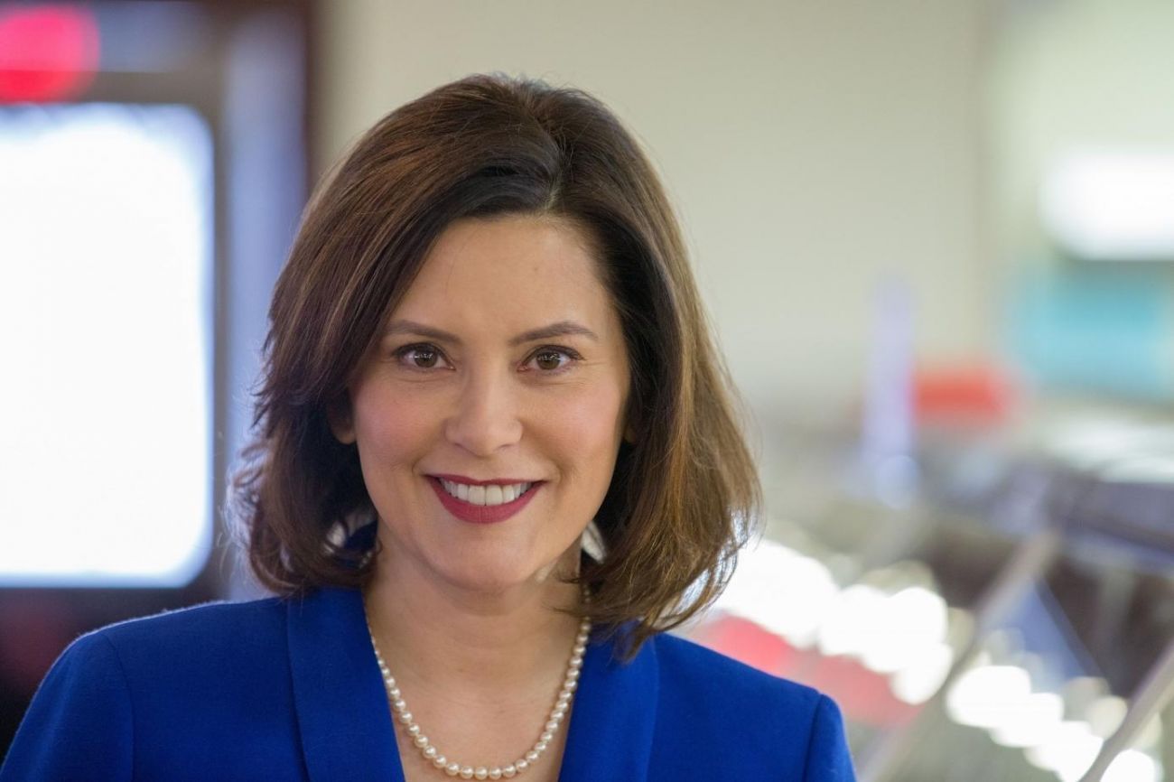 Gretchen Whitmer wearing a blue suit and pearl necklace with a smile on her face