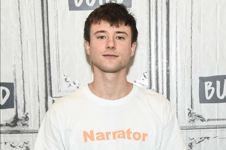 Alec Benjamin wearing a white t-shirt with an inscription that says Narrator