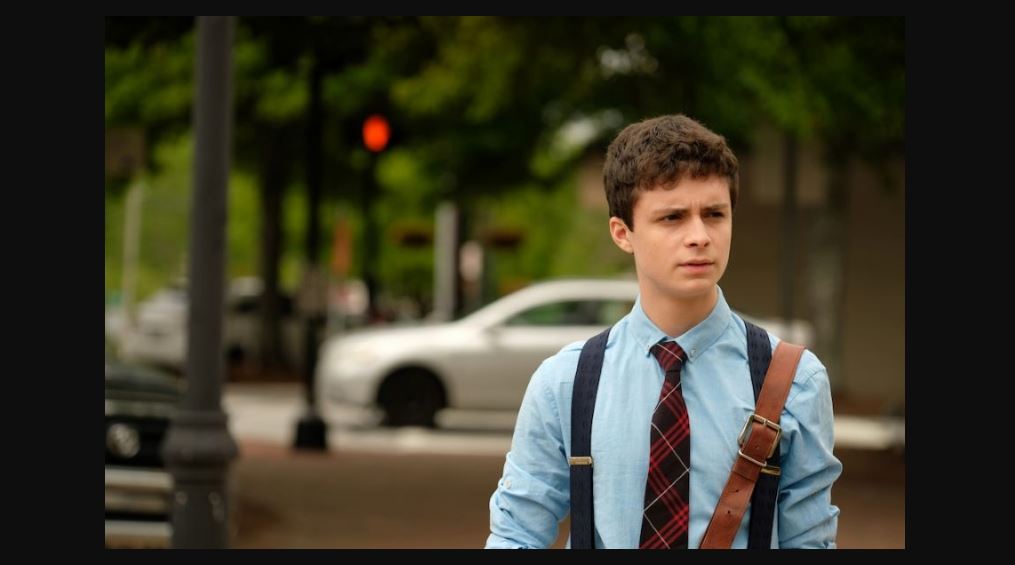 Lucas Jade Zumman wearing a blue shirt with a tie in a movie scene