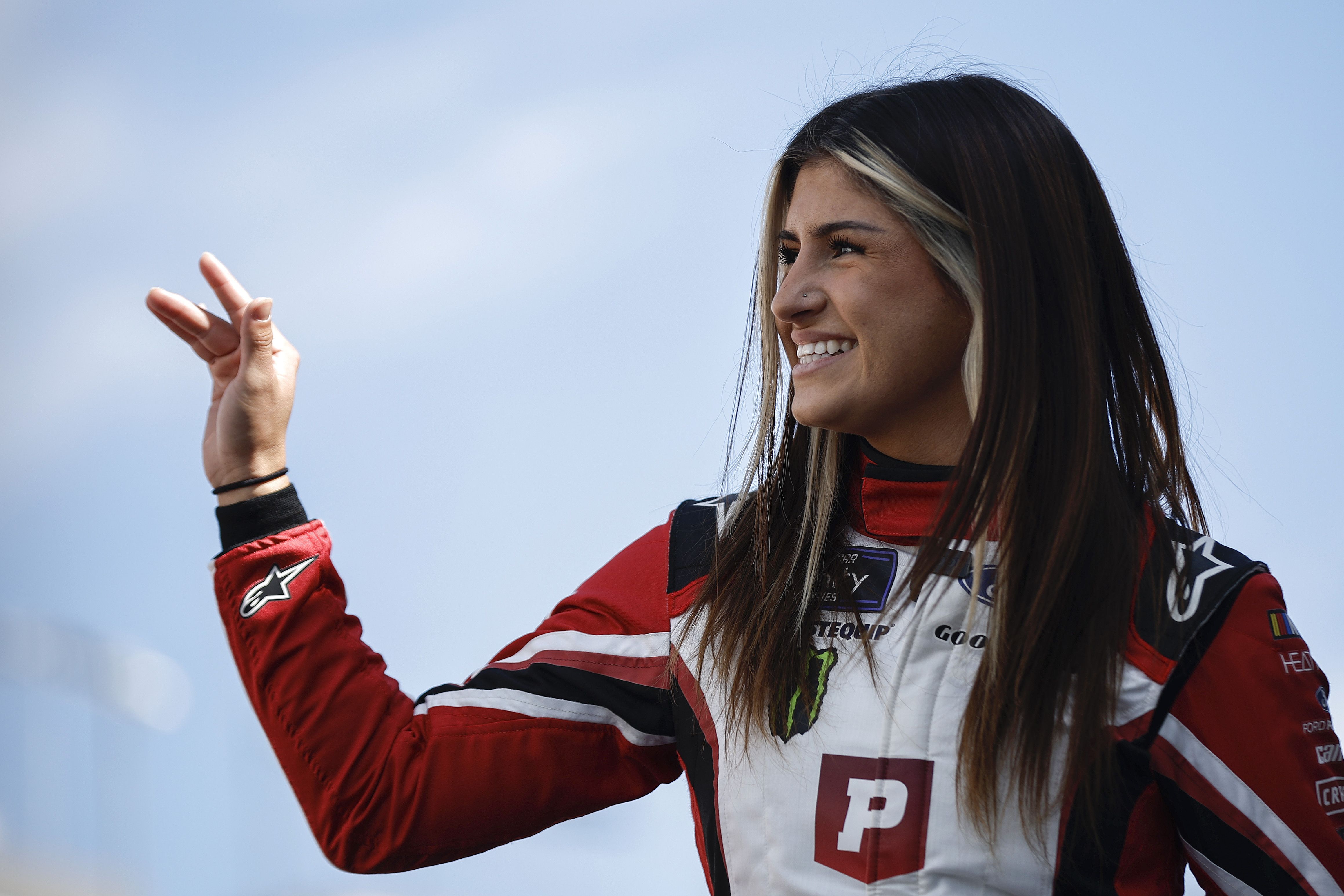Hailie Deegan wearing her racing attire as she waves her hand