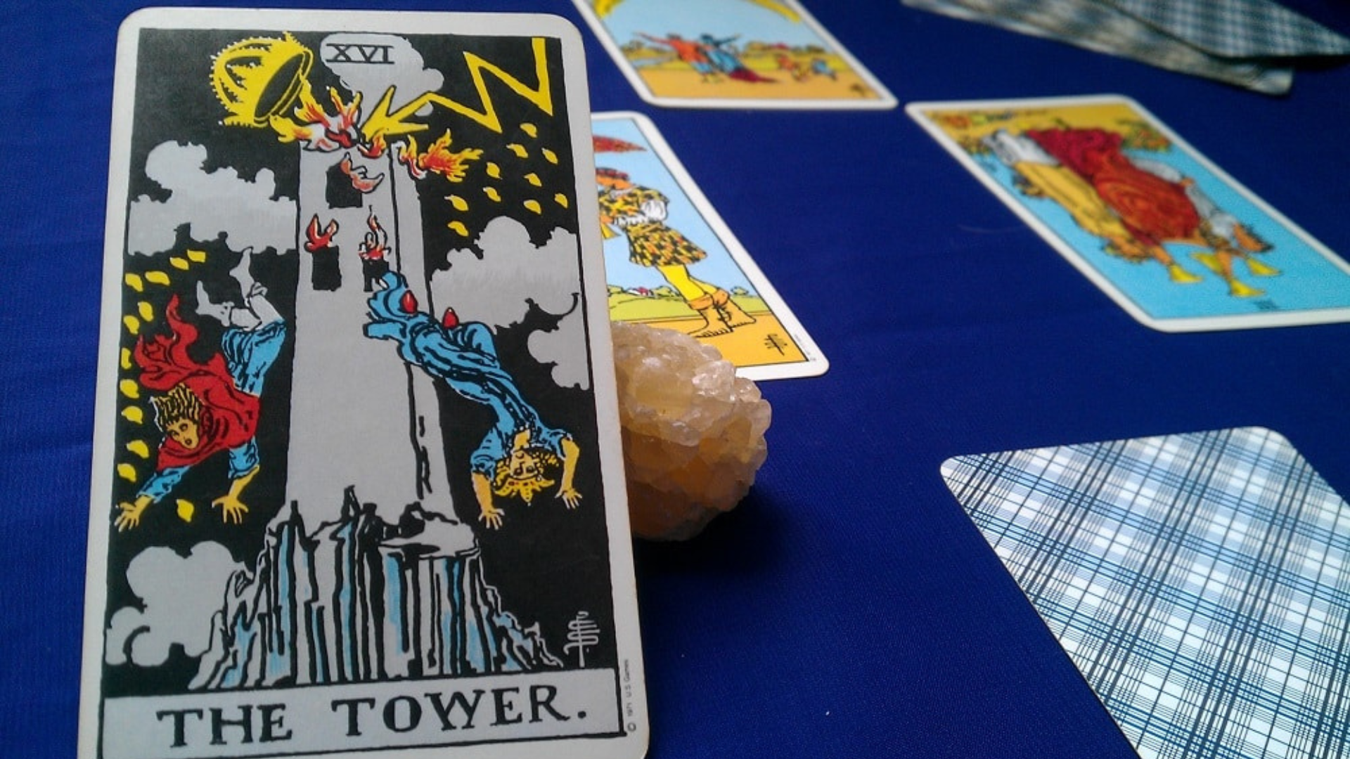 A tower tarot card placed on a blue table along with other cards and a crystal