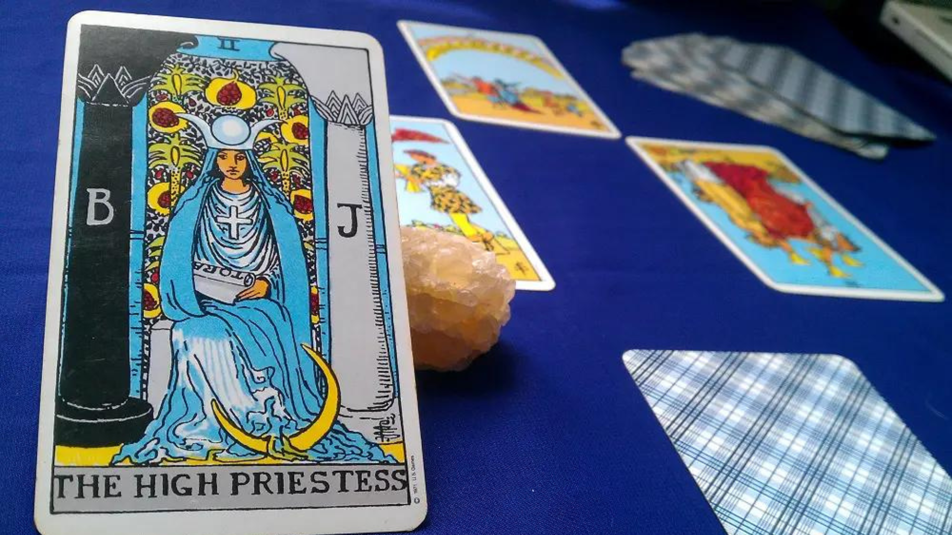 A  High Priestess Tarot Card placed on top of a blue table along with other tarot cards and a crystal