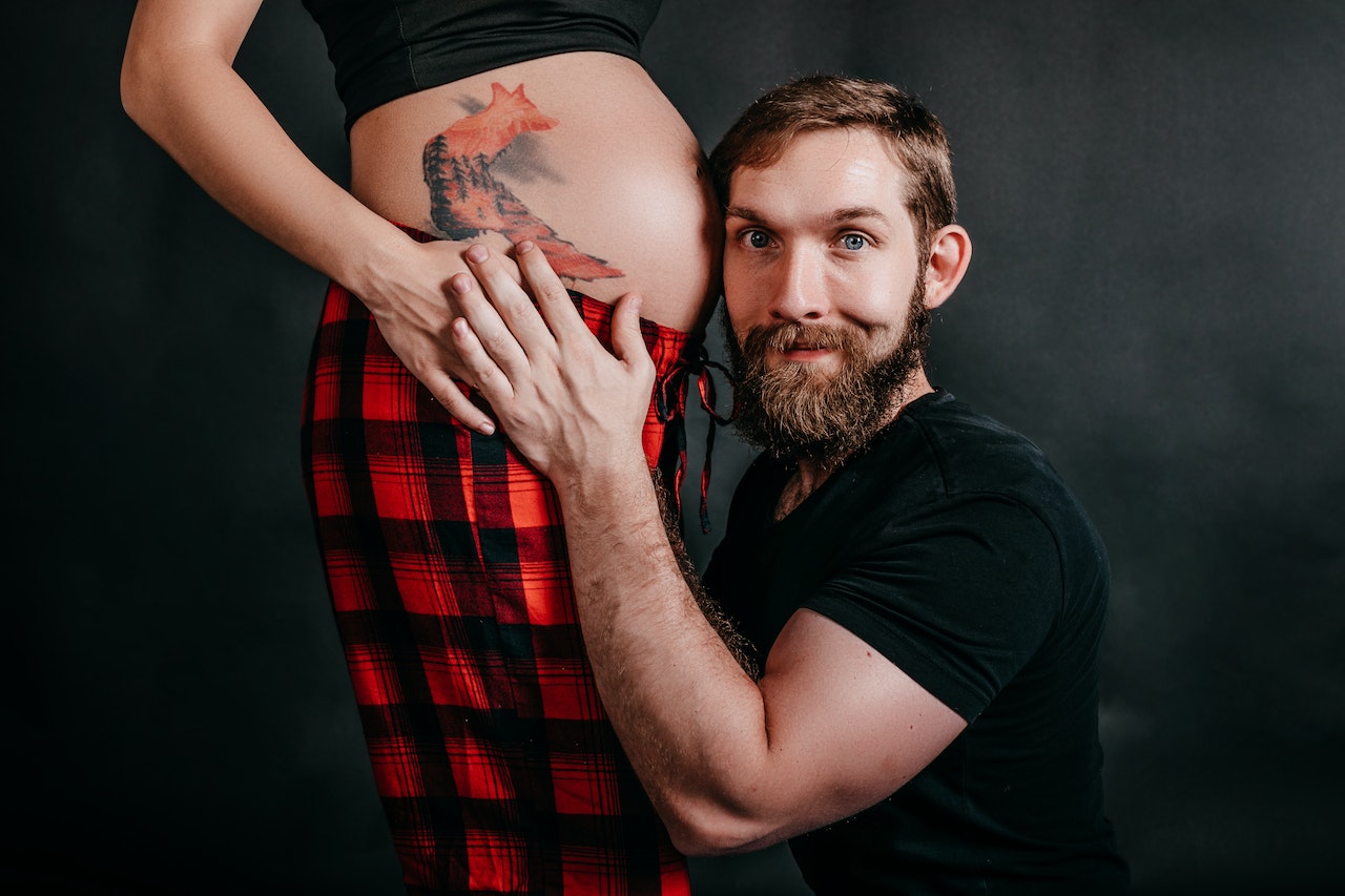 Man embracing faceless pregnant partner on black background