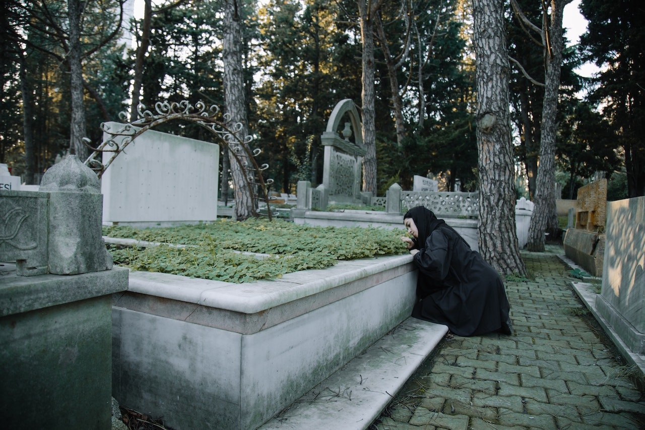 Mournful woman leaning on grave in cemetery