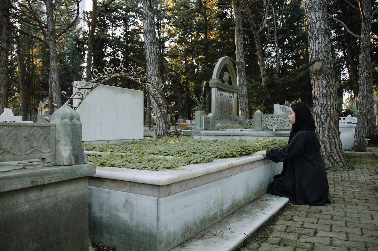 Sorrowful woman touching grave on pavement in cemetery