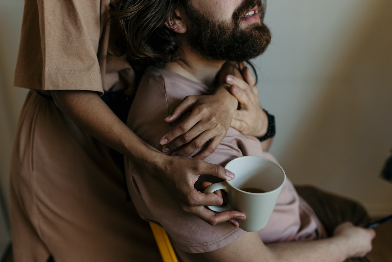 Arms hugging man from behind with one hand holding an almost empty cup