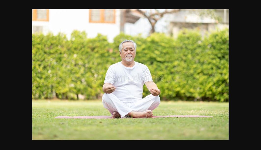 An old man with eyes closed wearing all white in a yoga position on a yard with green grass