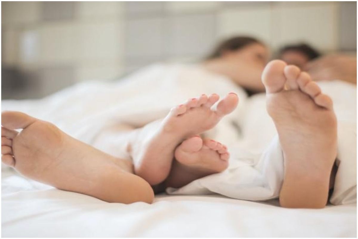 The feet of a man and a woman laying on a bed covered with a white duvet with their faces blurred in the background