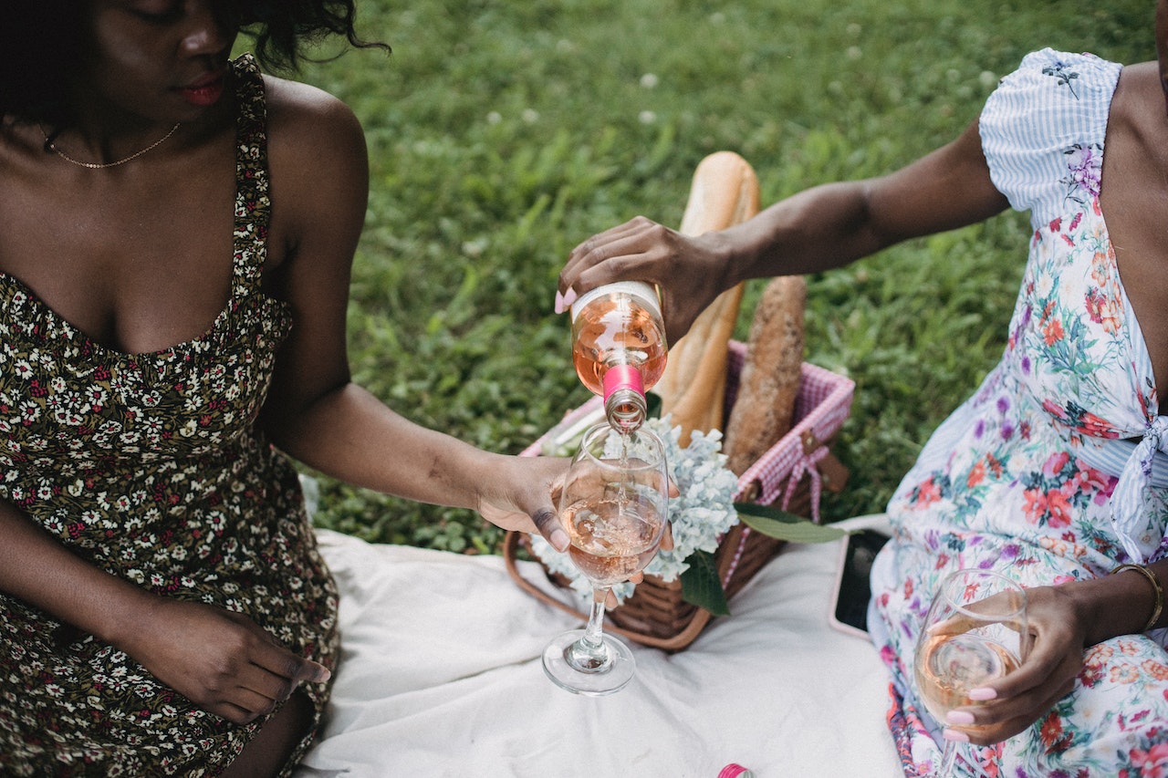 Two African American women on a picnic, with one pouring non-alcoholic wine to the other