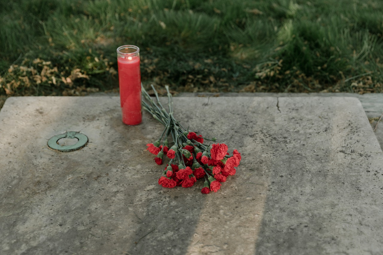 A Red Candle and Red Bouquet of Flowers on a Gravestone