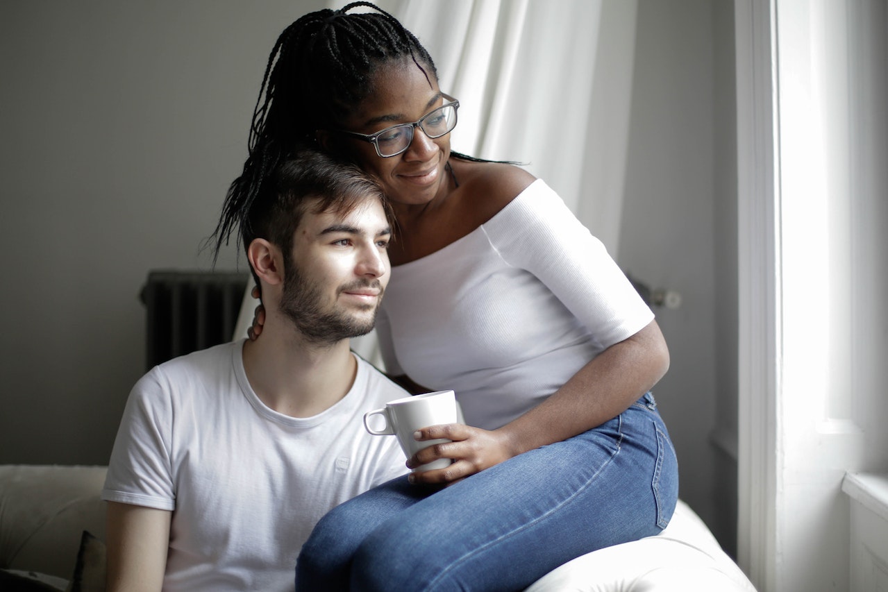 Cheerful multiethnic couple resting on sofa and looking through window at home