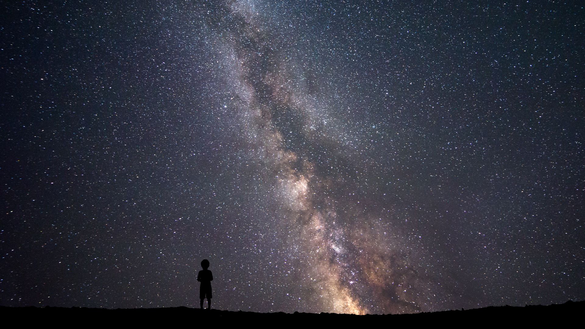 A little boy standing on a cliff while looking at the milky way