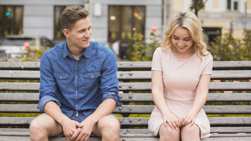 A man and a woman sitting on a bench outdoors while smiling at each other