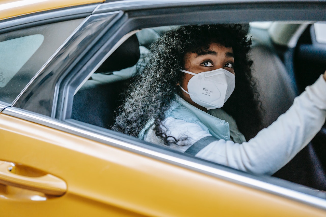 A female with a mask riding in a yellow car