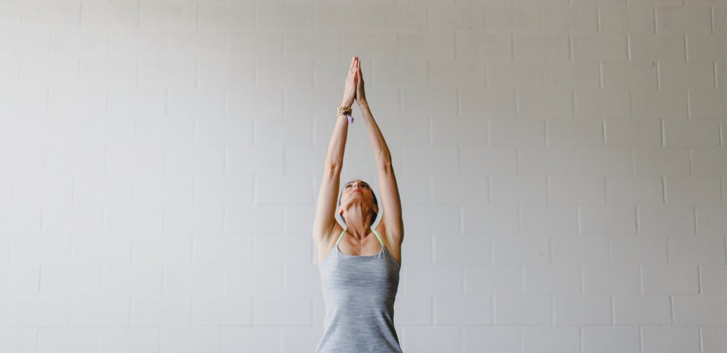 A woman sitting in a yoga position with her two hands joined together in the air