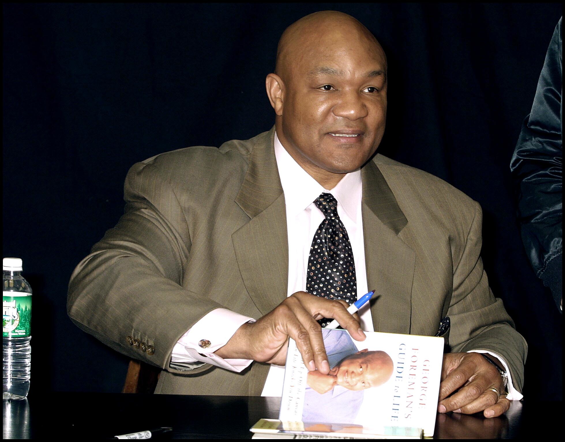 George Foreman wearing a light green coat while holding a book