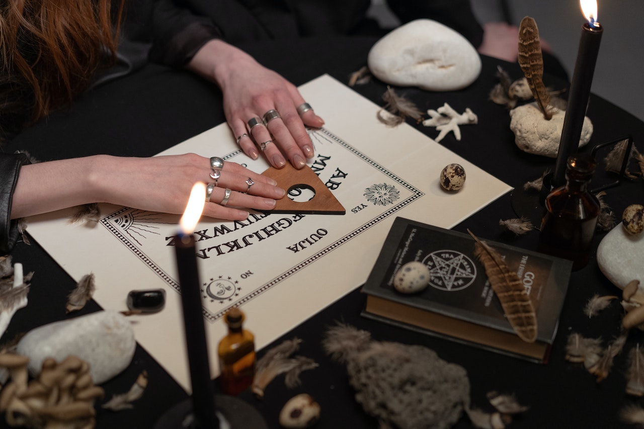Hands of Women on a Ouija Board Near Burning Candles