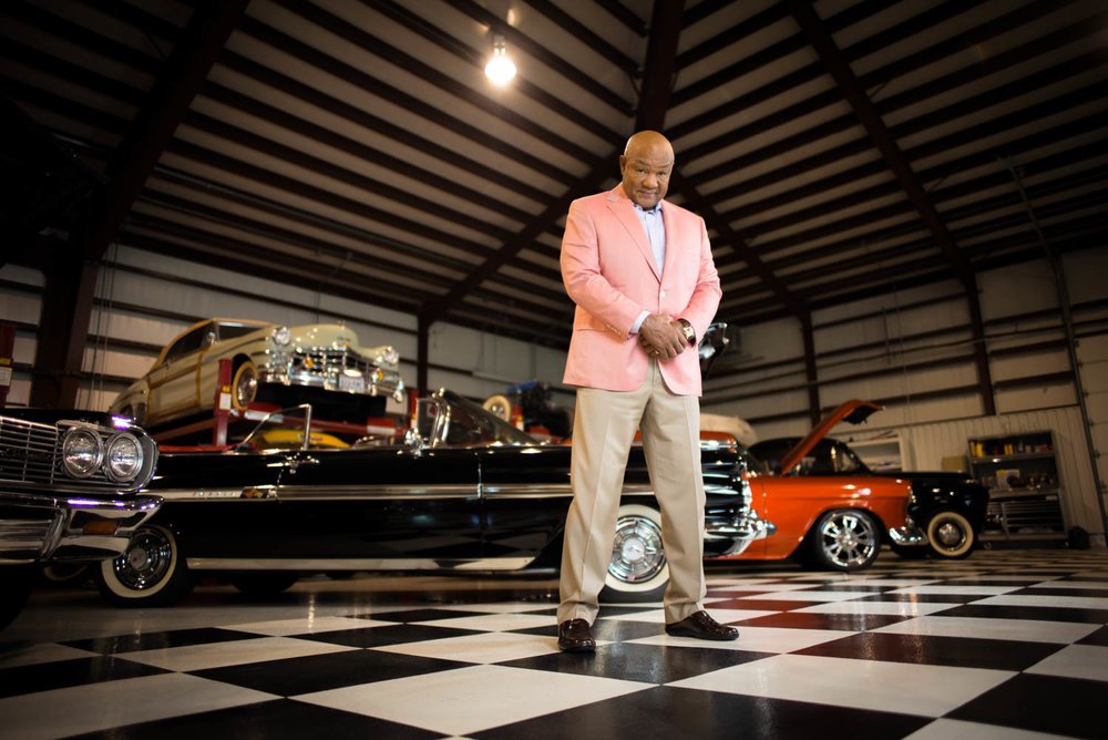 George Foreman wearing a pink coat with cars behind it