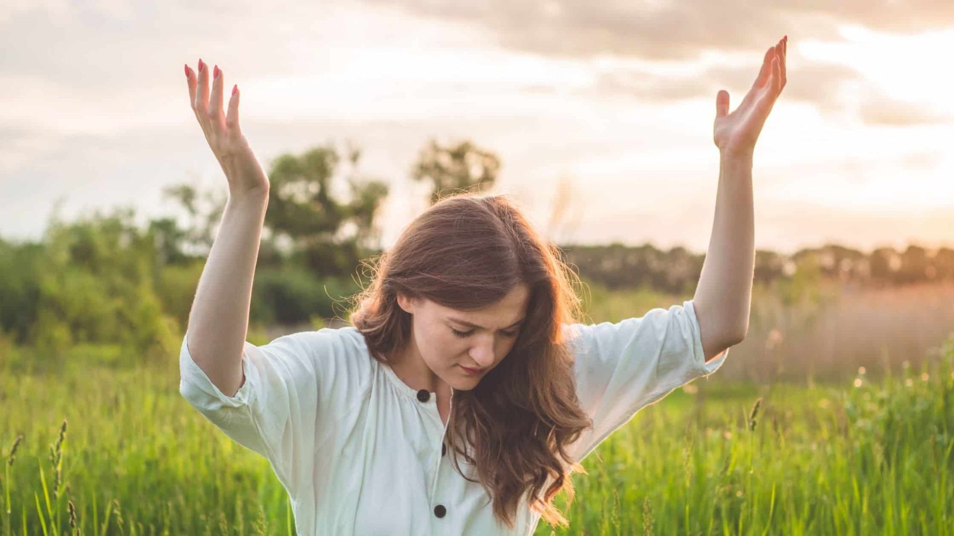 Woman Standing In A Field With Hands Lifted To The Sky In Prayer