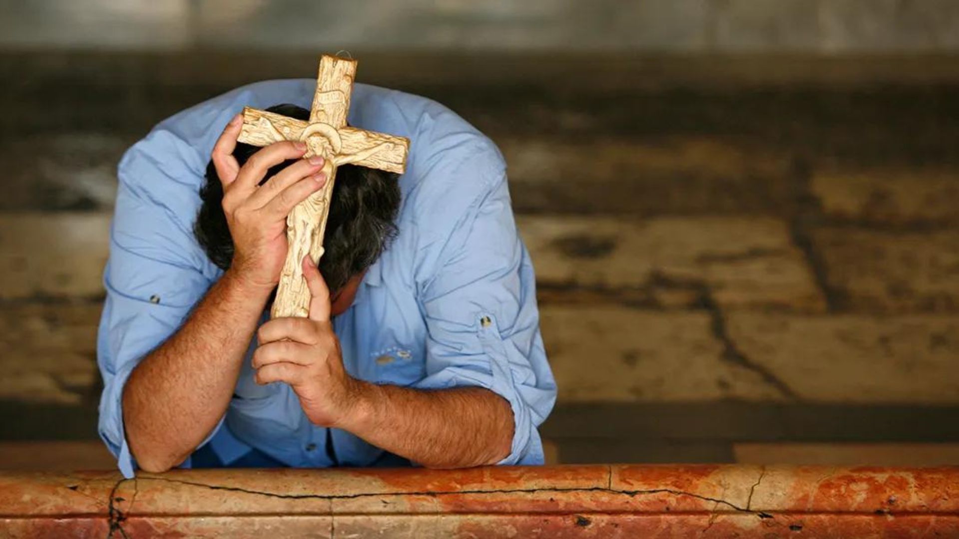 A Man Praying While Holding A Wooden Cross