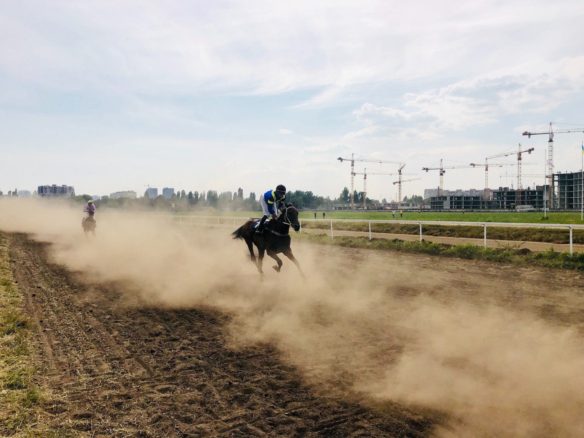 Two horses with riders are running on a muddy track.