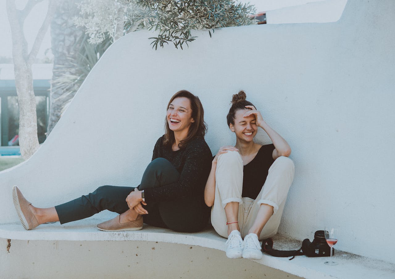 Two smiling Women Sitting on White Bench 