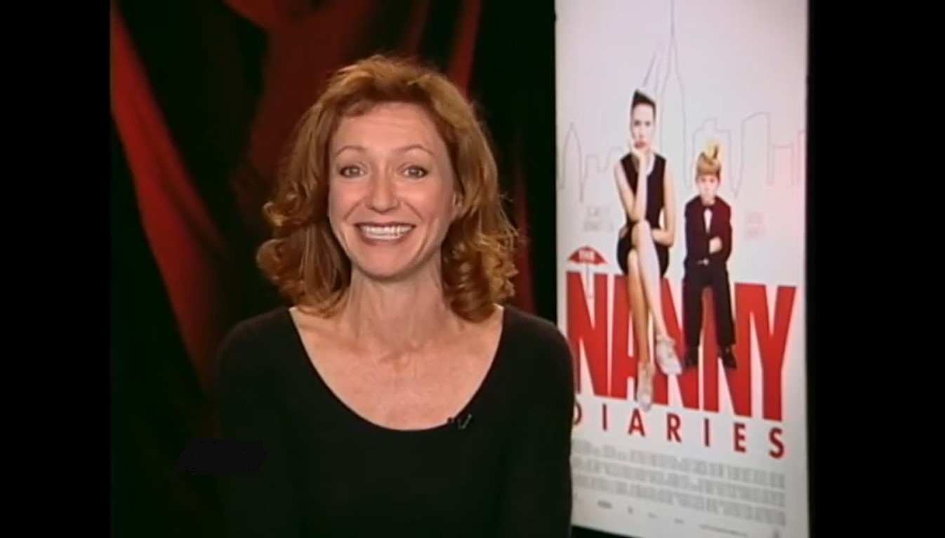 A grinning Julie White in black long sleeve top beside a movie poster with the words ‘Nanny Diaries’