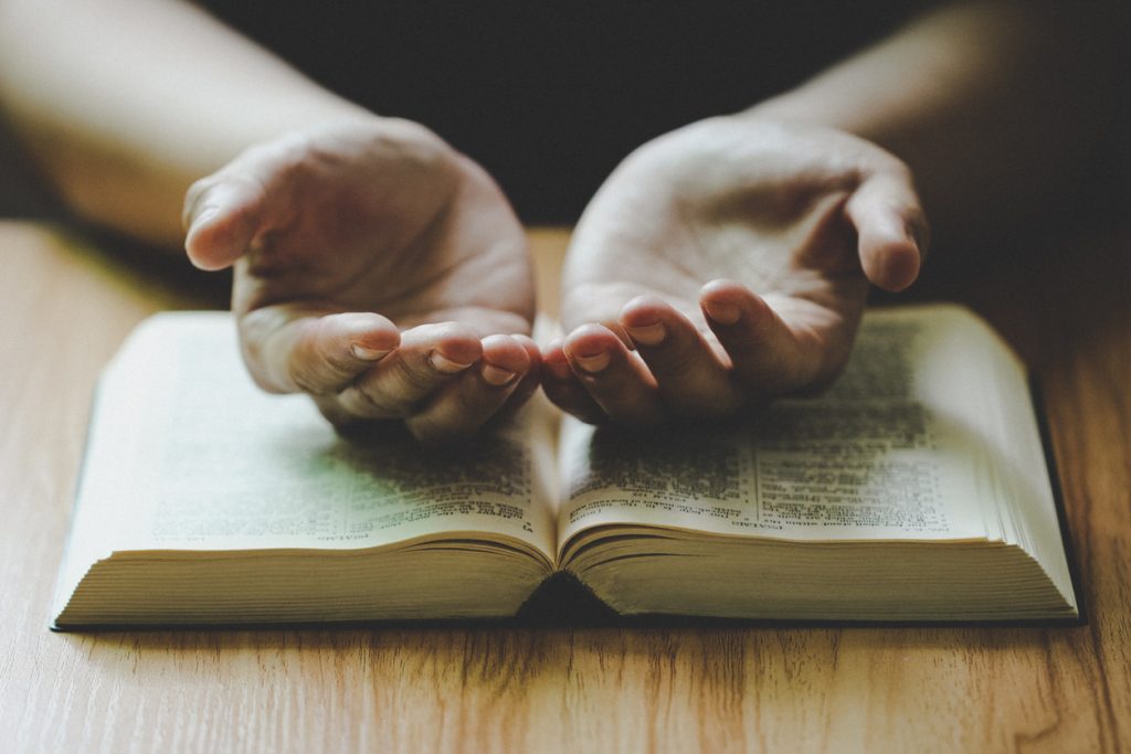 A person's hands open in prayers on a Bible