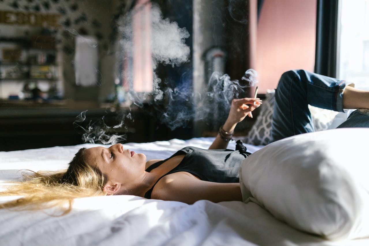 A Woman in Black Tank Top Lying on the Bed while Smoking Weed