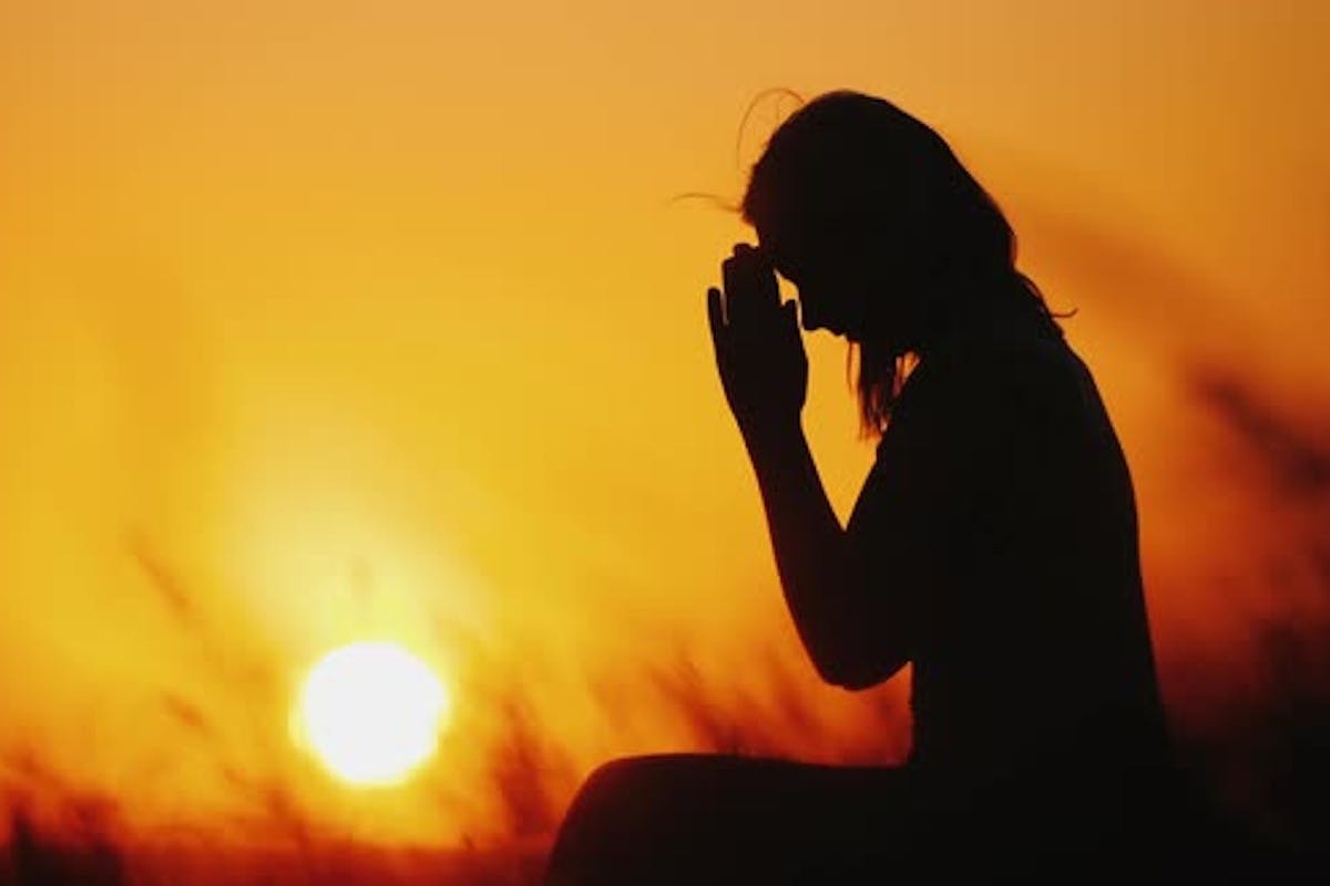 Silhouette of a Woman Praying Against the Background of an Orange Sky