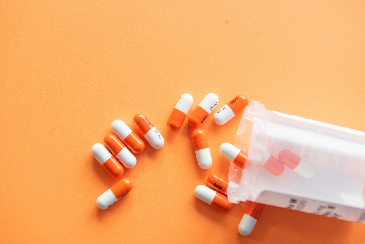 Fifteen orange-and-white medicine capsules spilling out of an overturned transparent pill bottle
