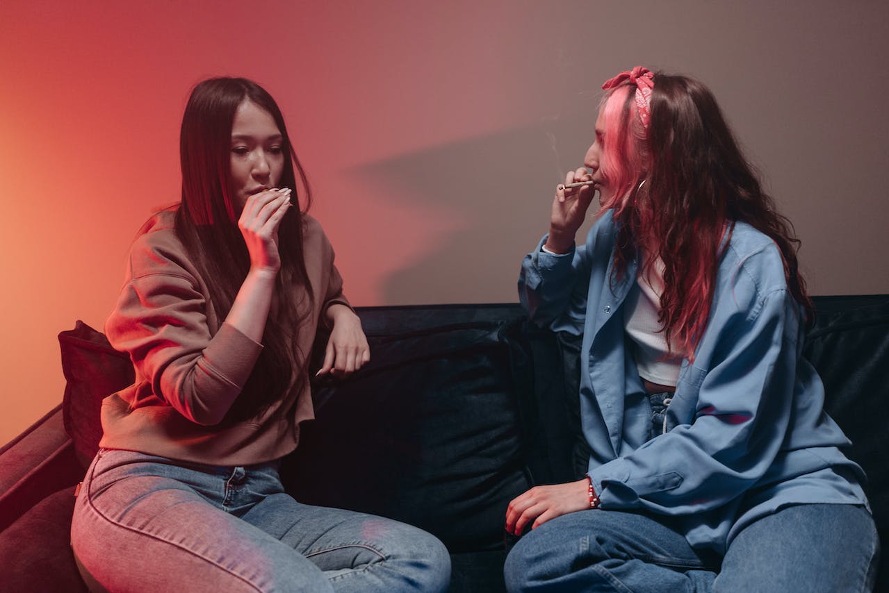 Two Women Sitting on Black Couch Smoking Marijuana