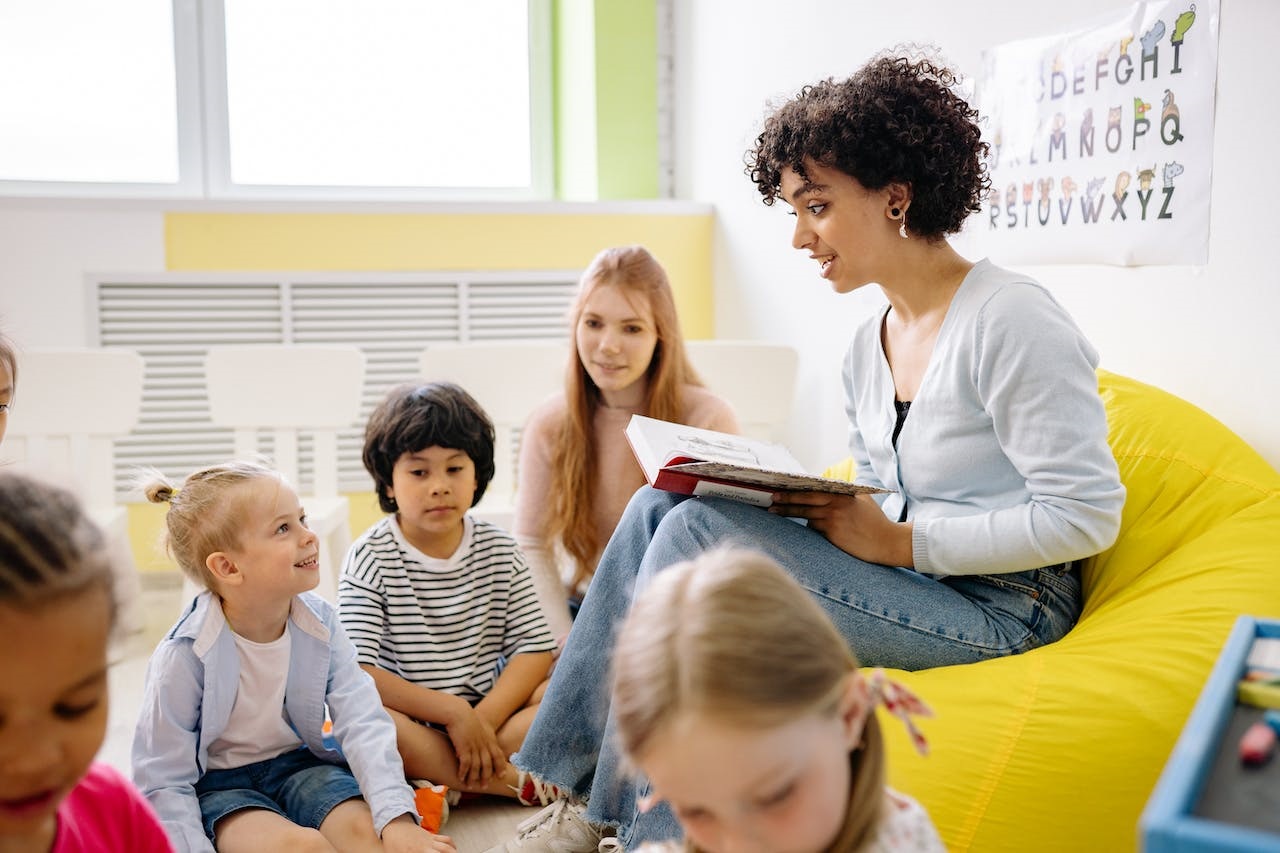 A female elementary teacher reading a book to female ADHD students, with female assistant teacher beside her